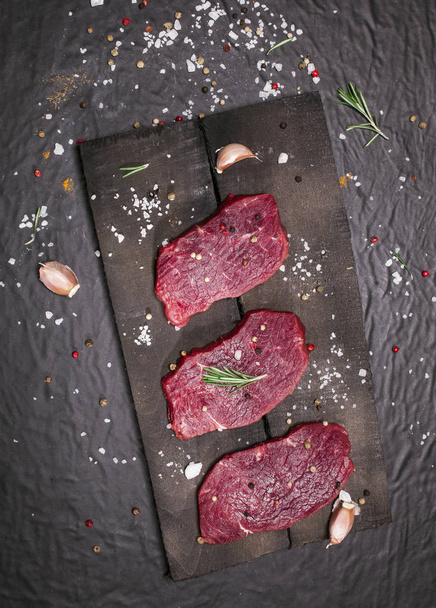 Raw beef steak on a cutting board with rosemary and spices. - Fotografie, Obrázek