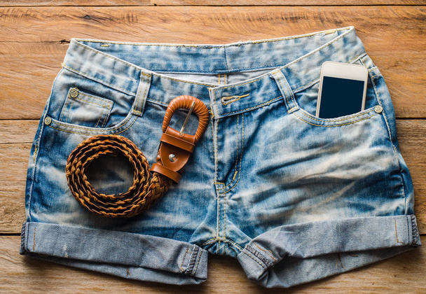 Šortky Jeans a chytrý telefon na dřevěnou podlahu. - Fotografie, Obrázek