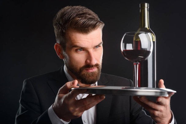 Sommelier examining red wine. Young professional lifted the tray against a light to analyze quality of beverage. Selective focus. - Foto, afbeelding