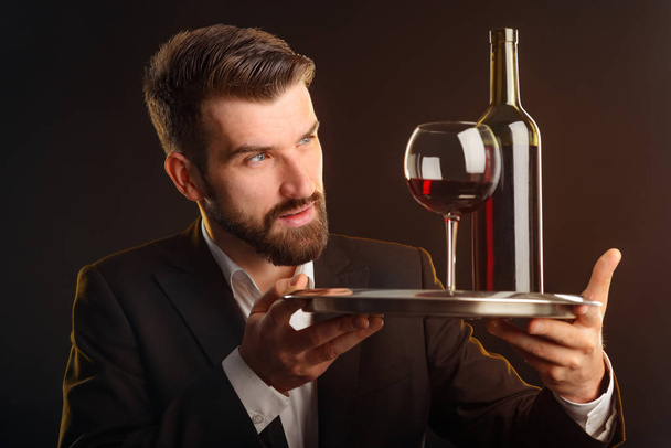 Concentrated man tasting red wine. Expert gazing at beverage to note the color and other its properties. Closeup shot with dark background and orange lighting. - Foto, afbeelding