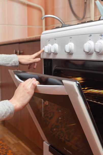 Close up van vrouwen hand openen van de deur van de oven om te controleren het gebraad in de gas-kookplaat. - Foto, afbeelding