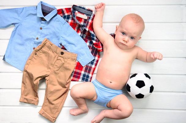 Baby on white wooden background with clothing  and football toy. - Photo, Image