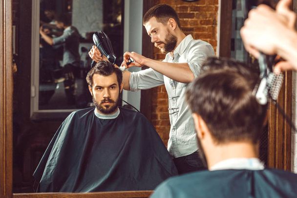 Young handsome barber making haircut of attractive man in barbershop - Photo, image