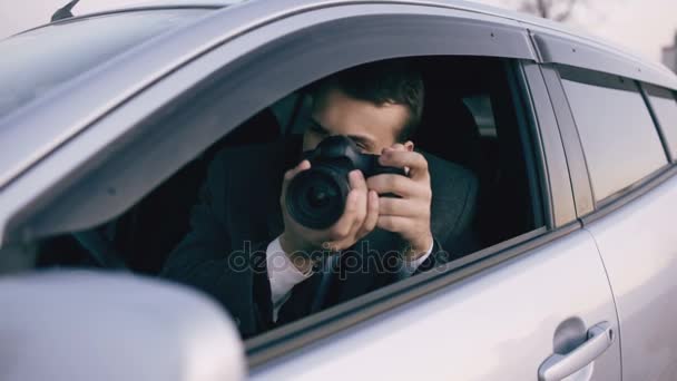 Mladí soukromý detektiv muž sedí uvnitř vozu a fotografování s fotoaparátem dslr - Záběry, video