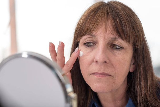 Donna mettendo crema anti-età sul suo viso
 - Foto, immagini