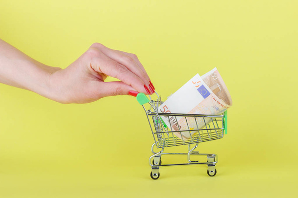 Fifty euro in the shopping pushcart, yellow background - Photo, Image