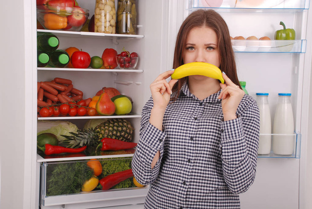 Mladá dívka drží banán na ústa, imitující úsměv. - Fotografie, Obrázek