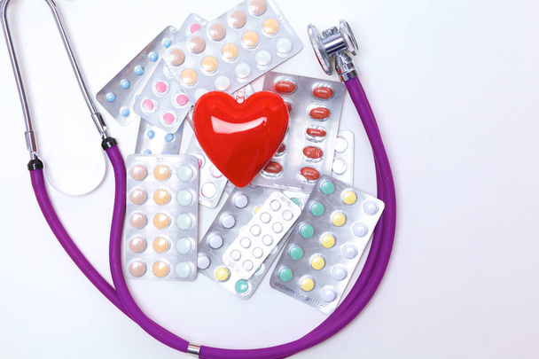 Крупный план таблеток, разбросанных по столу со стетоскопом и лежащим рядом сердцем
 - Фото, изображение