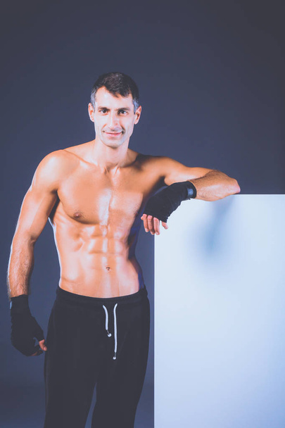 Strong athletic man standing near board on black background - Photo, Image