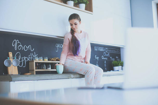 Young woman sitting on table in the kitchen - Foto, imagen