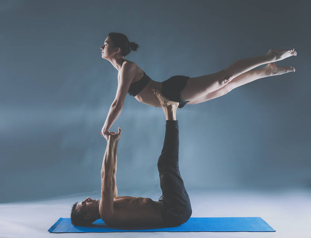 Young couple practicing acro yoga on mat in studio together - Foto, afbeelding