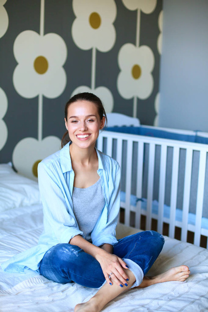 Young woman sitting on the bed near childrens cot - Photo, Image