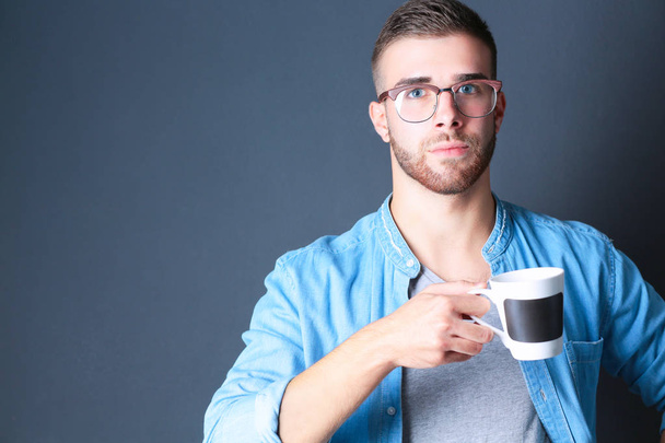 Portrait handsome young man standing and holding cup of coffee in his hands - Φωτογραφία, εικόνα
