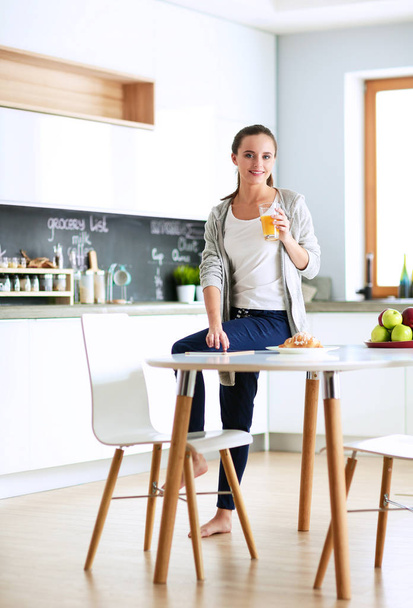 Young woman with orange juice and tablet in kitchen - Fotoğraf, Görsel