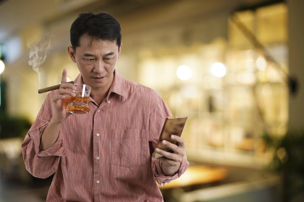 Man holding glass of whiskey with cigarette and looking mobile p - Fotoğraf, Görsel
