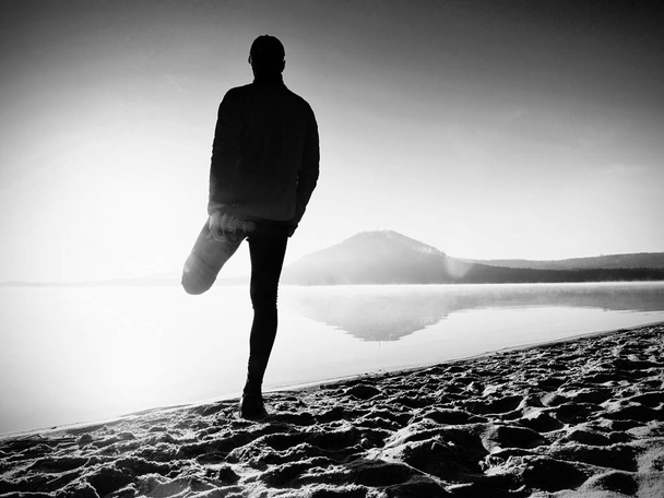 Hombre haciendo ejercicio en la playa. Silueta del hombre activo haciendo ejercicio y estirándose en el lago
 - Foto, imagen