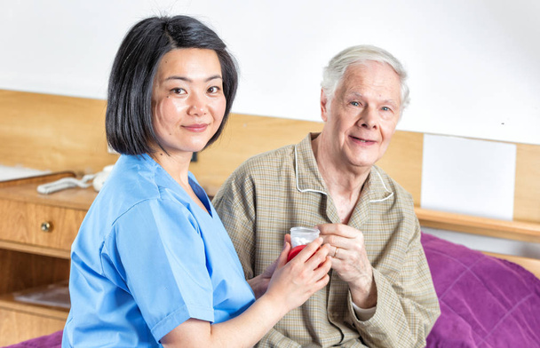 Krankenschwester verabreicht älteren Mann Pille im Krankenhausbett - Foto, Bild