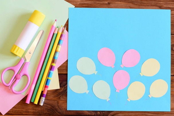Creating a paper card with balloons. Step. Tutorial for children. Air day or birthday card concept. Card with balloons, scissors, glue stick, colored paper, pencils on a table. Children art activity - Fotó, kép