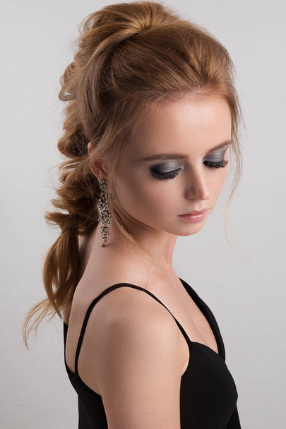 Portrait of blondes with a highly assembled tail in a black decollete dress with closed eyes and silvery eyeshadows - Foto, Imagen