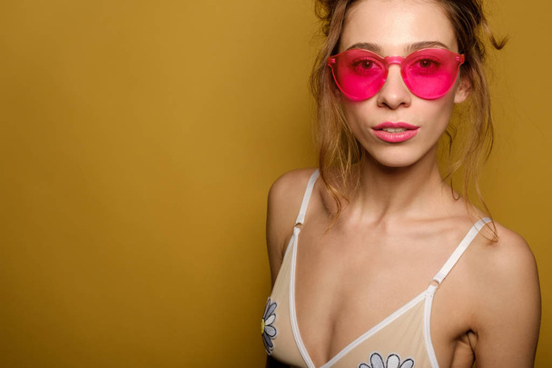 Closeup portrait of a girl in an amusing swimsuit, jeans, with carelessly gathered hair and pink glasses. - 写真・画像