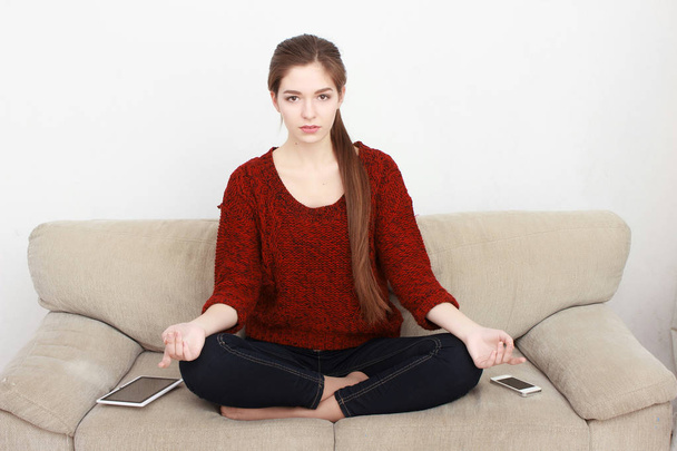 woman meditating in lotus position on the couch - Foto, afbeelding