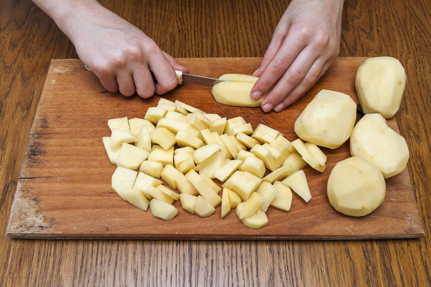 Woman's hand with a knife cutting slicing potatoes on wooden boa - 写真・画像