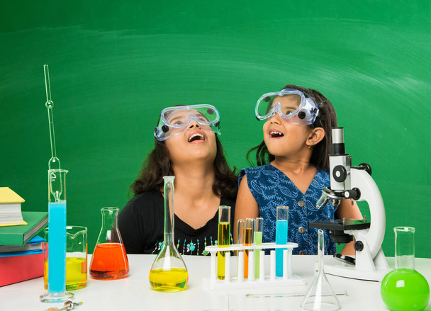 2 милые маленькие индийские девочки проводят научный эксперимент или проект в классе с зеленой доской с научными рисунками
 - Фото, изображение