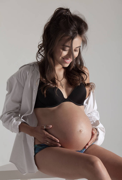 glücklich schwangere Frau mit Händen auf dem Bauch isoliert über grauem Hintergrund - Foto, Bild