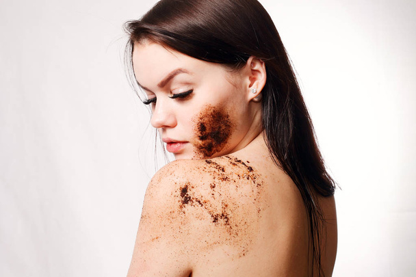 Brunette woman cleans the skin of the body coffee scrub - Фото, изображение