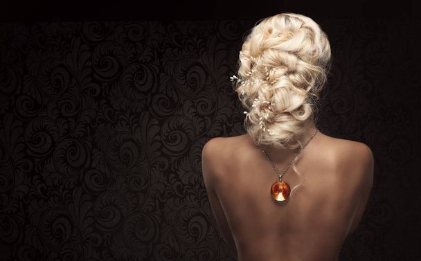 Naked beautiful blond unrecognizable woman with professional hairstyle wearing necklace with orange gem, backside - Photo, image
