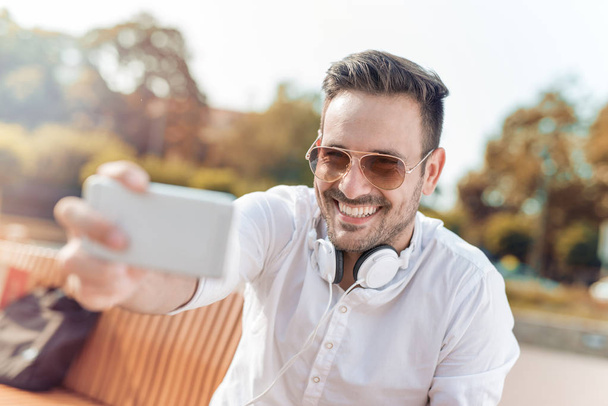 Χαρούμενος νεαρός άνδρας ακούει μουσική σε ένα έξυπνο τηλέφωνο - Φωτογραφία, εικόνα
