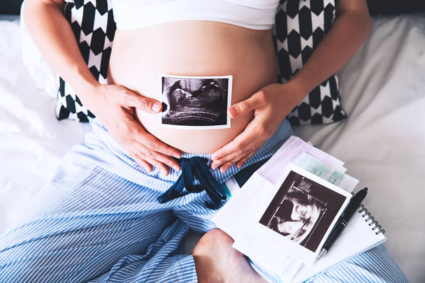 Pregnant woman makes notes in notebook and holding ultrasound im - Φωτογραφία, εικόνα