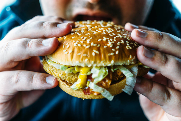 hungriger dicker Mann hält Hamburger und beißt zu - Foto, Bild
