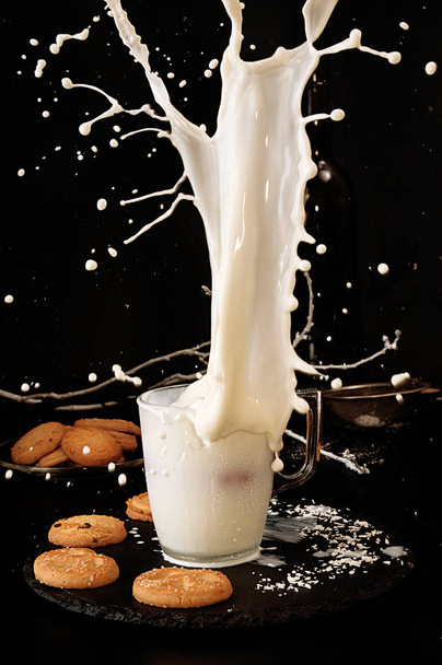 fallende Kekse zu einem Glas Milch mit Spritzer auf schwarzem Hintergrund - Foto, Bild