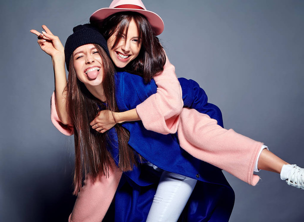 fashion portrait of two smiling brunette women models in summer casual hipster overcoat posing on gray background. Girls holding each other on back  - Φωτογραφία, εικόνα