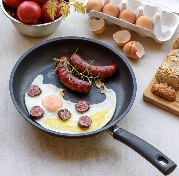 Fried sausages and eggs in a pan served with bread, tomatoes and egg shell, TOP VIEW - Zdjęcie, obraz