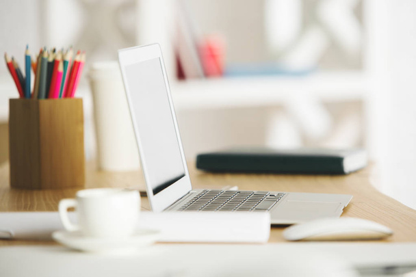 Close up de desktop de escritório desfocado com laptop em branco, xícara de café e suprimentos. Mock up, conceito de espaço de trabalho
 - Foto, Imagem