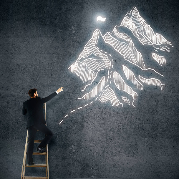 Rückansicht eines jungen Mannes auf Leiter, der Berge mit Fahne auf weißem Hintergrund zeichnet. Siegerkonzept - Foto, Bild