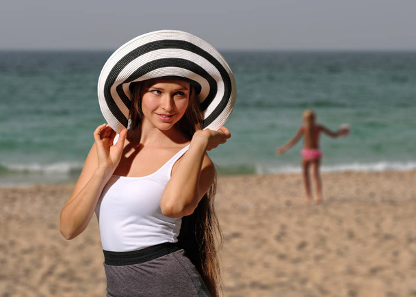 Красивая молодая женщина в белой футболке и шляпе на пляже
 - Фото, изображение