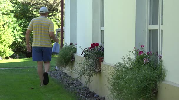 ο άνθρωπος πότισμα λουλουδιών σε κατσαρόλα που κρέμονται στον τοίχο του σπιτιού το καλοκαίρι. 4k - Πλάνα, βίντεο