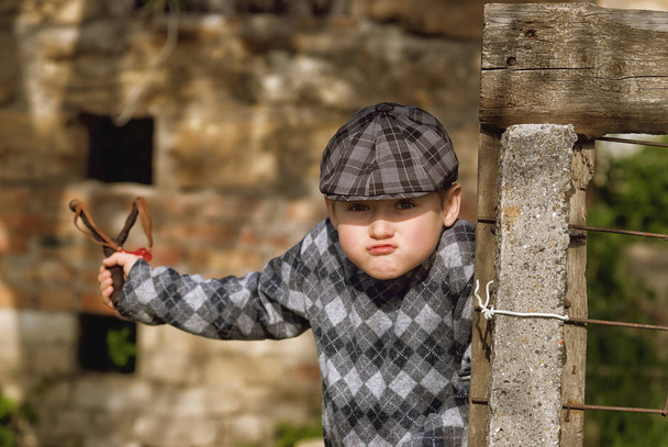 Маленький мальчик в кепке, хулиган с рогаткой в руках
 - Фото, изображение