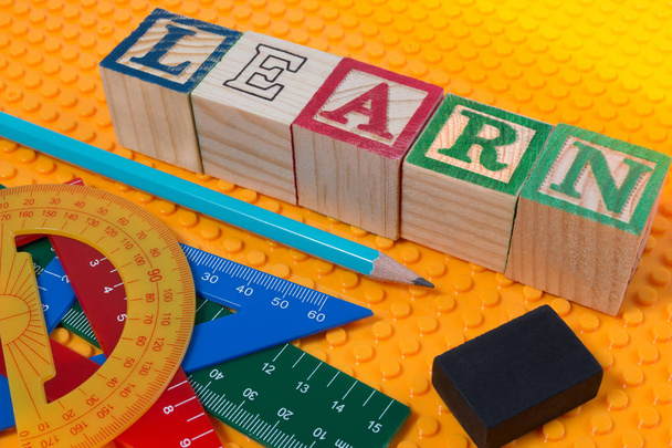 Слово LEARN, написане в дерев'яному кубі на жовтому пластику з шкільними канцелярськими інструментами
. - Фото, зображення