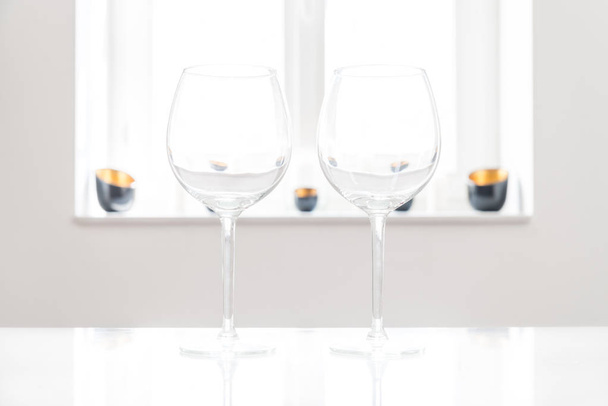 Two empty red wine glasses on white table with white background and window - Foto, Imagem