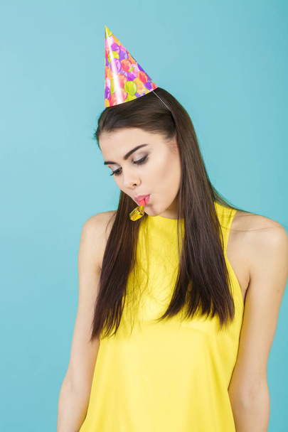 young attractive smiling woman with birthday hat and whistle on blue background. celebration and party - Foto, afbeelding