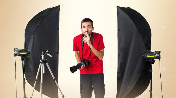 Fotógrafo en su estudio haciendo un gesto de silencio en la espalda ocre
 - Foto, Imagen