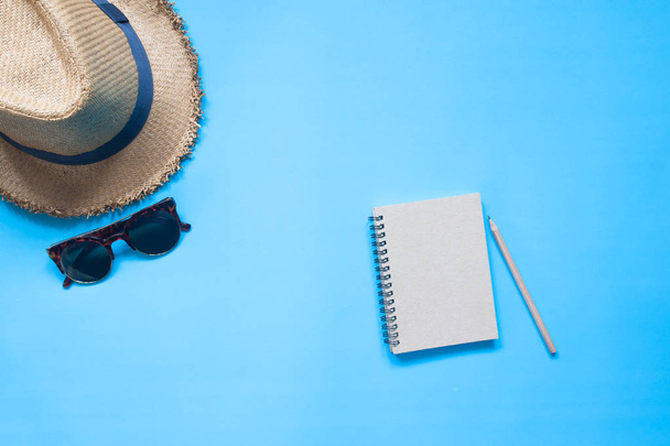 Flat lay of notebook with pencil, hat and sunglasses on blue col - Φωτογραφία, εικόνα