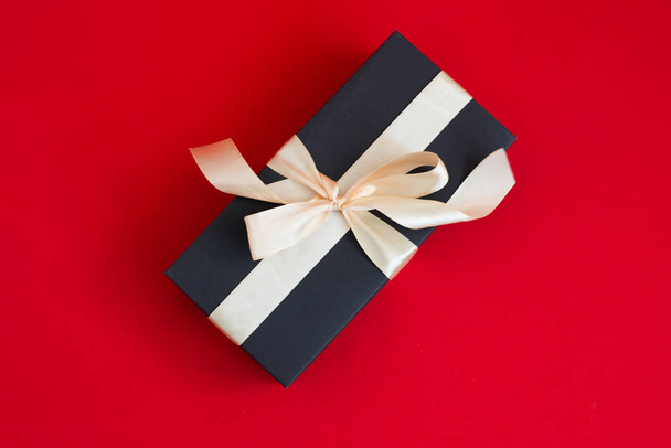 black gift box with gold ribbon and a bow on red background - Fotó, kép