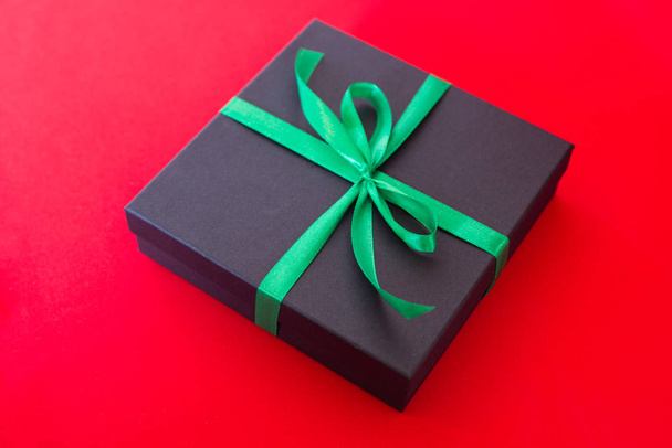 black gift box with green ribbon and a bow on red background - Foto, Imagem