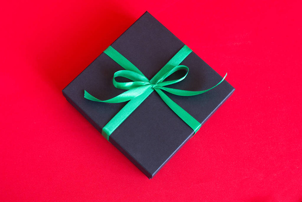 black gift box with green ribbon and a bow on red background - Photo, image
