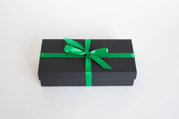 black gift box with green ribbon and a bow on white background - Valokuva, kuva